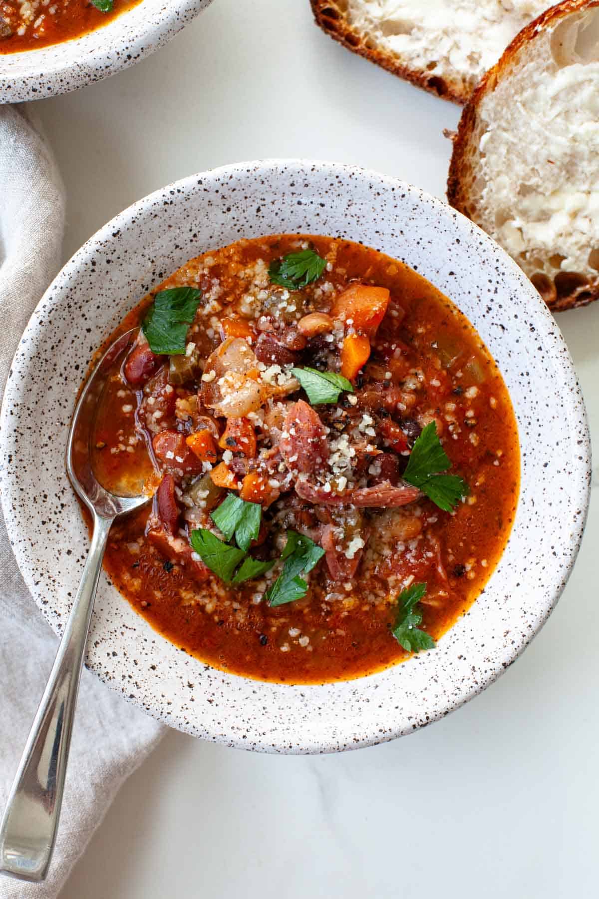 white speckled bowl filled with Instant Pot 15 Bean Soup that is garnished with freshly cracked black pepper, parmesan cheese and parsley 