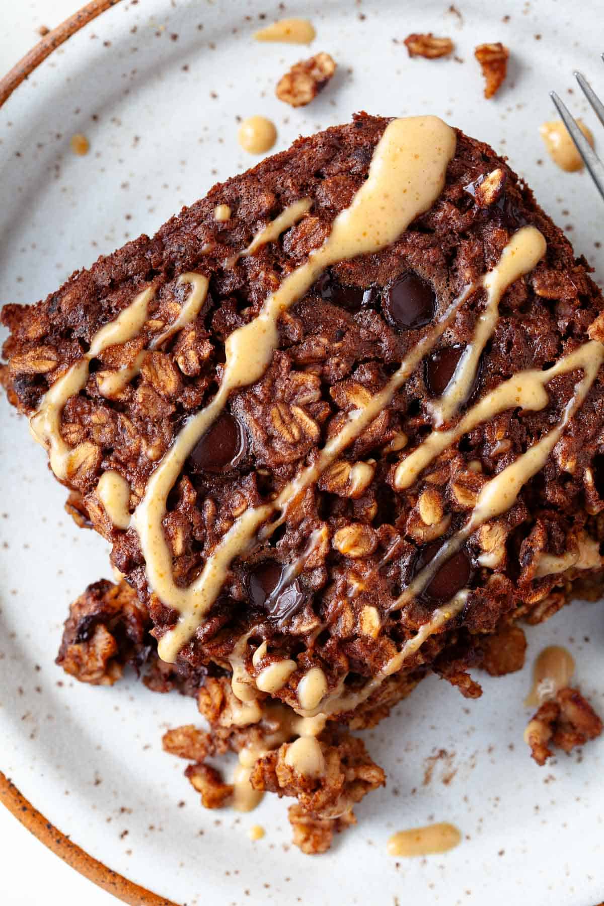 chocolate baked oatmeal on white speckled plate with chocolate chips and peanut butter drizzle.