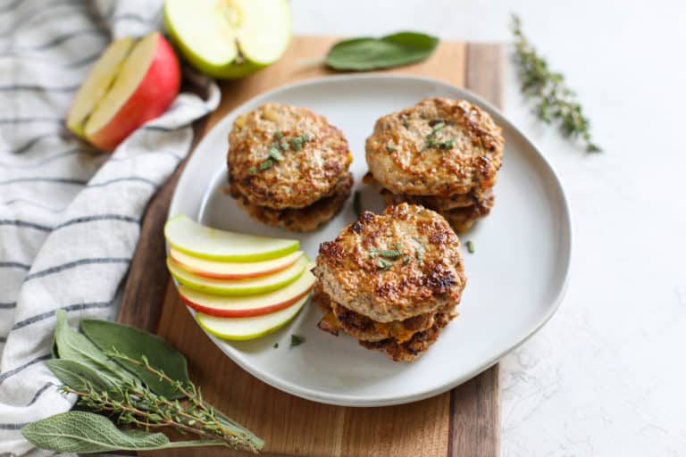 Turkey Apple Sausages stacked on a white plate next to apple slices. 