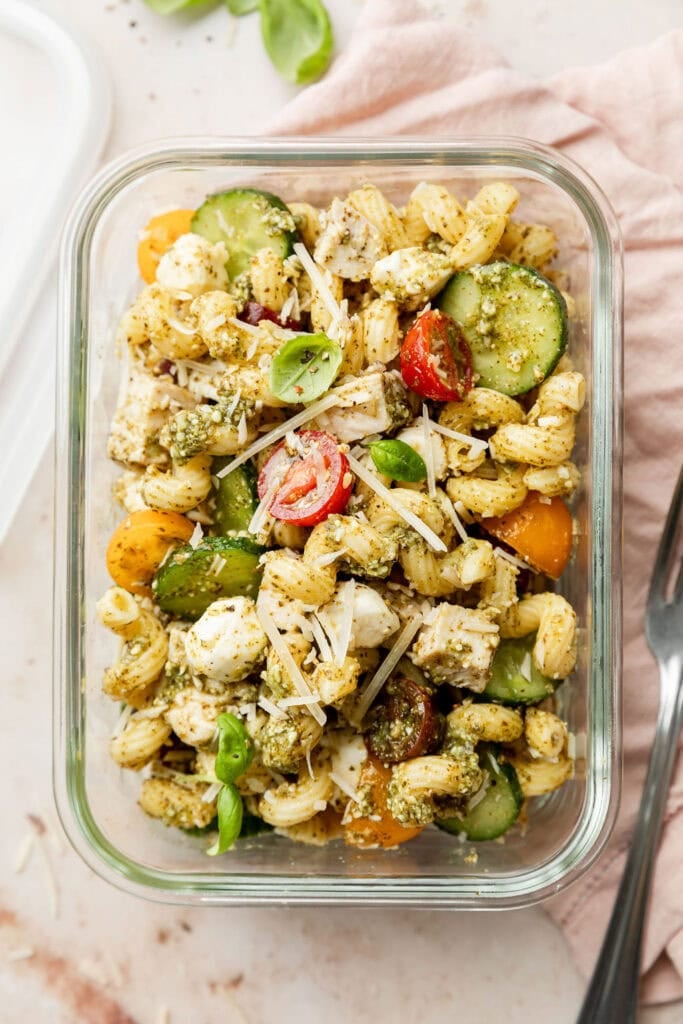 Overhead view glass meal prep container filled with a serving of pesto pasta salad