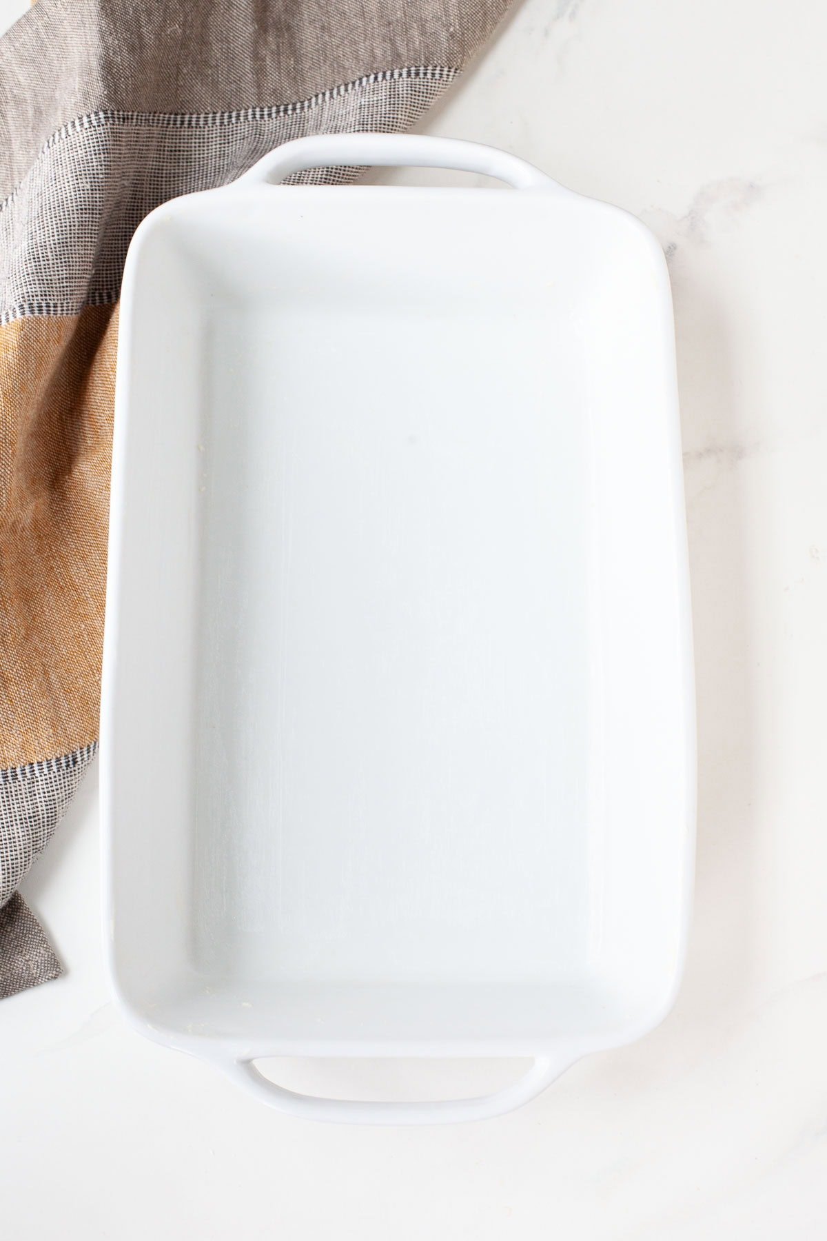 empty white baking dish on marble surface beside kitchen towel