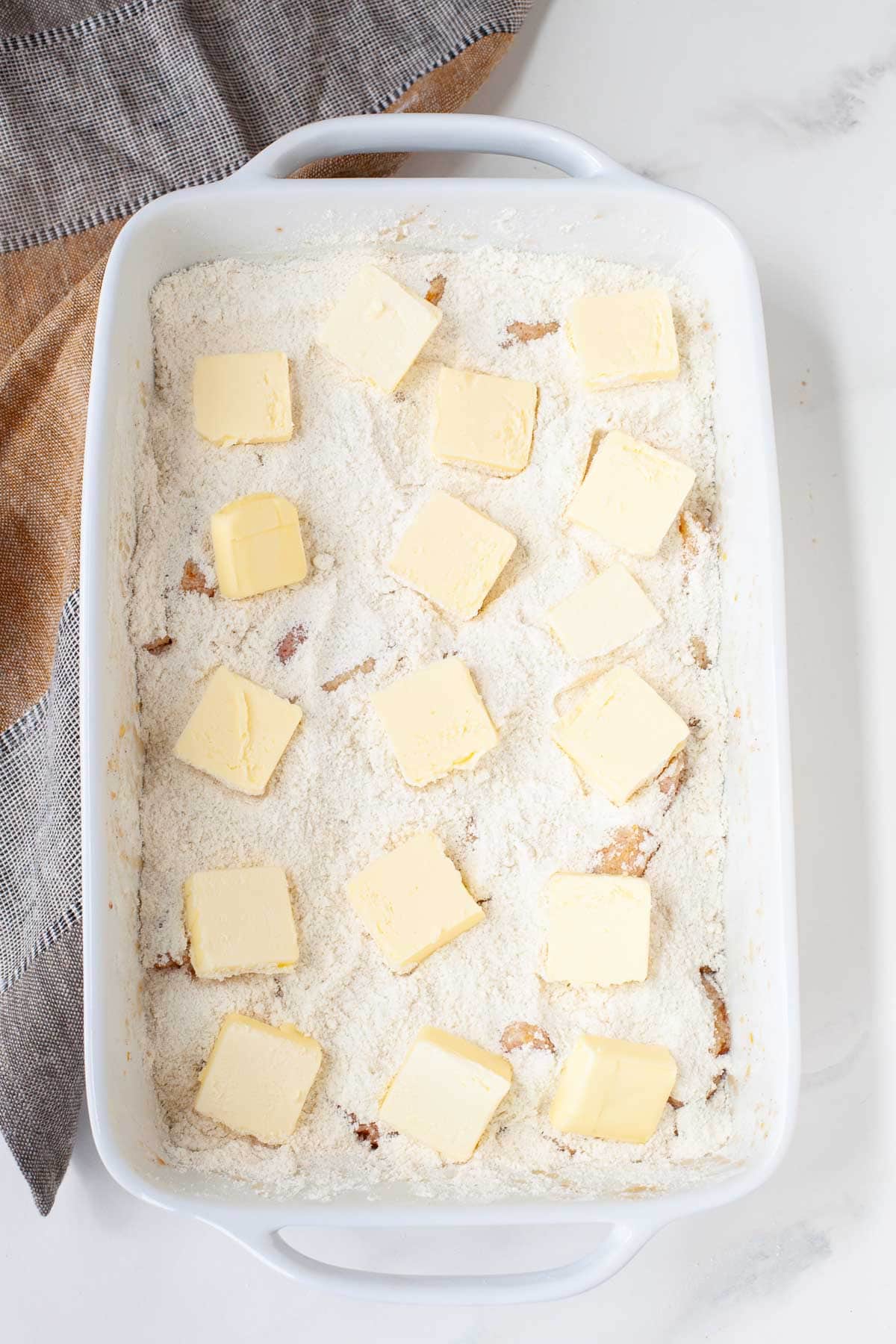 white baking dish with cake mix peach cobbler prior to baking on marble surface