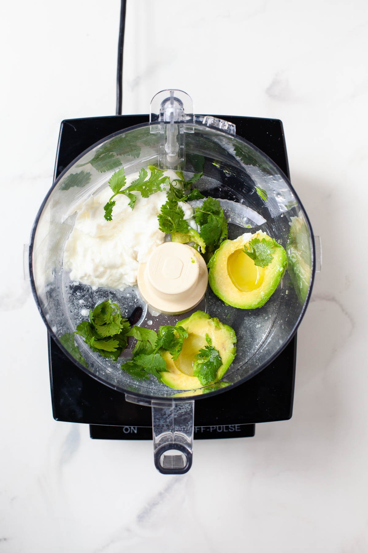 avocado, greek yogurt, cilantro and lime juice in food processor on white marble surface