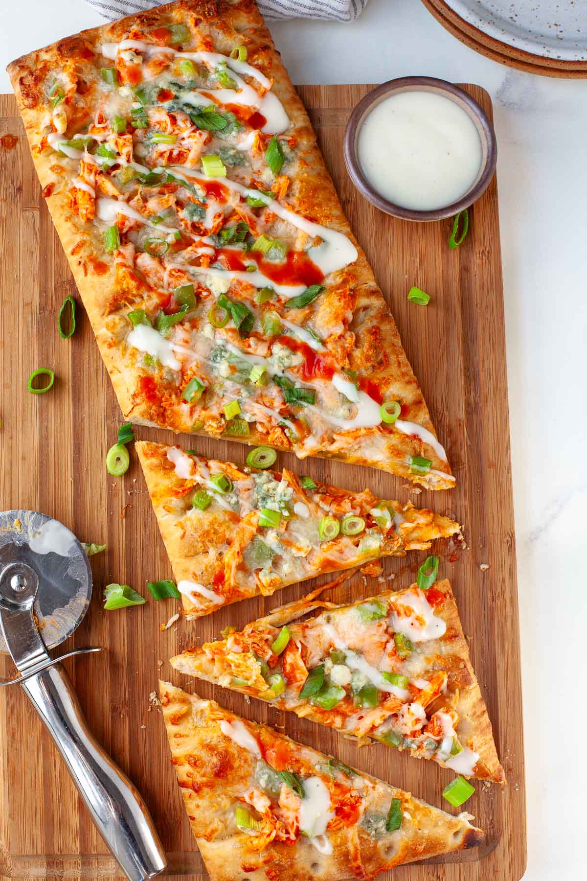 buffalo chicken flatbread with three slices cut on wood cutting board next to small bowl with ranch dressing