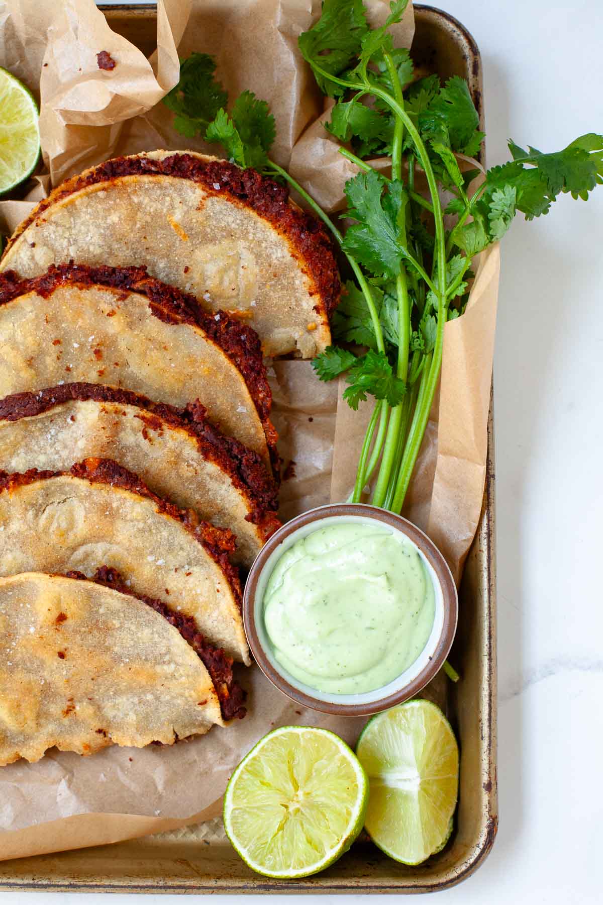 close up of crispy black bean tacos with avocado lime crema, sliced lime, and cilantro